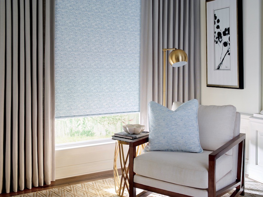 Chair and floor lamp near roller shades over window